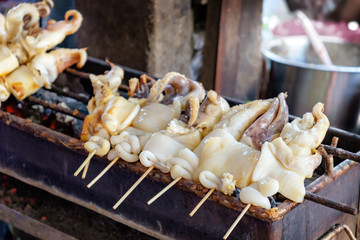 Fresh Squid on skewers is being grilled by a street vendor in the most famous flea market in Chinatown district, Bangkok, Thailand
