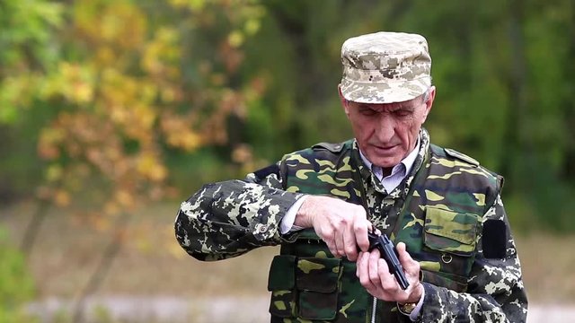 Soldier in military uniform shoots a revolver. Retired officer at shooting range. Senior man in military uniform shoots a pistol in forest. Man with black gun