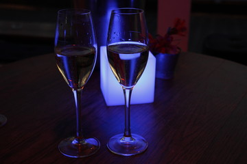 Two glasses of champagne in front of a blue light cube in a champagne lounge at night