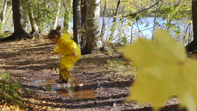 Little girl in a yellow rubber suit is jumping in a puddle.  Slow Motion