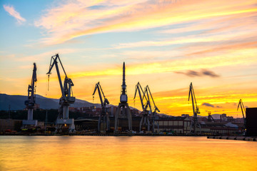 Obraz premium silhouetted cranes at dusk at shipyard