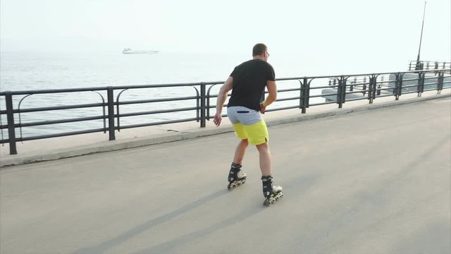 Young sporty man learns to roller skate and jump on waterfront 4K
