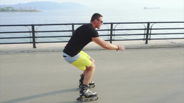 Young sporty man learns to roller skate and jump on waterfront 4K