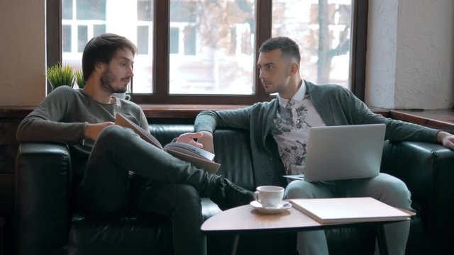 Two entrepreneurs working and taking notes together in table of a little office. Freelancer meeting, man with laptop drink coffee in coworking.