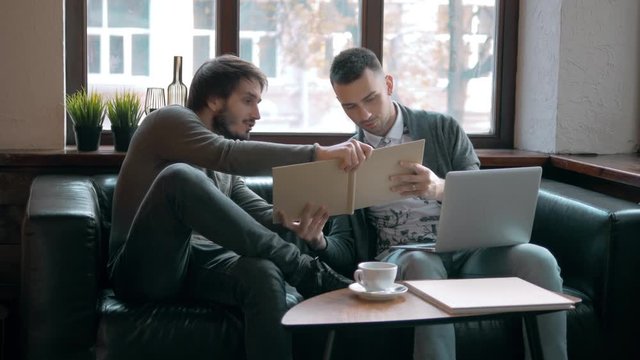 Two entrepreneurs working and taking notes together in table of a little office. Freelancer meeting, man with laptop drink coffee in coworking.
