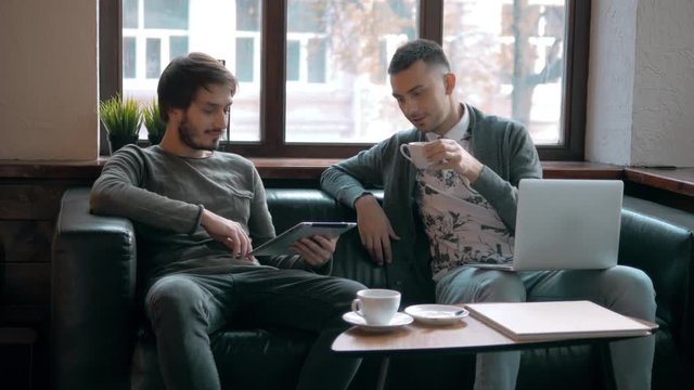 Two entrepreneurs working and taking notes together in table of little office. Freelancer meeting, man with laptop drink coffee in coworking.