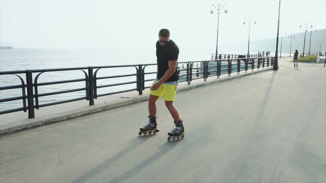Young sporty man roller skating on summer waterfront 4K
