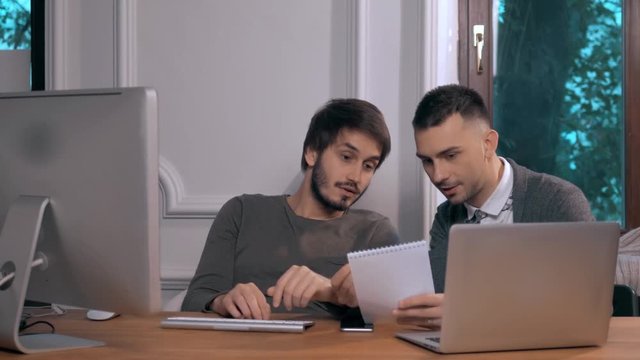 Young businessman explaining data to colleague at meeting, two freelancers work late