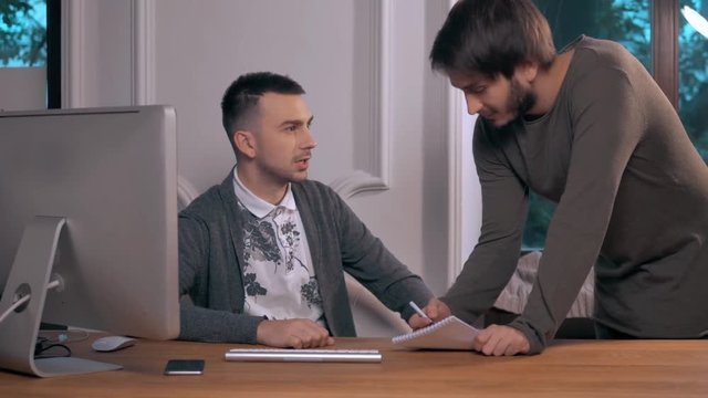 Young businessman explaining data to colleague at meeting, two freelancers work late