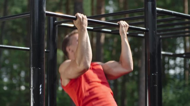 Muscular man doing chin ups on bar in the park in slow motion