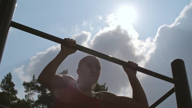 Low angle view of sporty woman doing pullover on bar outdoor at summer day