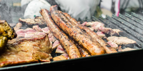 Argentina barbecue asado chorizo sausages and meat cooking on parilla grill at a street food market