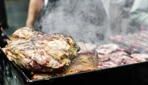 Argentina barbecue asado chorizo sausages and meat cooking on parilla grill at a street food market
