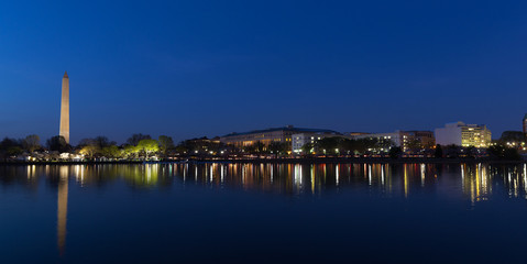 Night panorama of Washington DC during cherry blossom festival. Washington Monument and lights reflection in Tidal Basin waters.