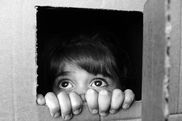 Face of afraid little girl peeking out from a cardboard box