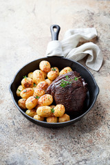 Roast beef and baked potatoes in cast iron frying pan, selective focus