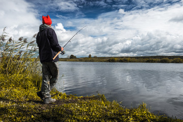 Fisherman standing on a coast of river with fishing rod