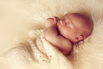 Sleeping newborn baby lying on white fur carpet covered with cre