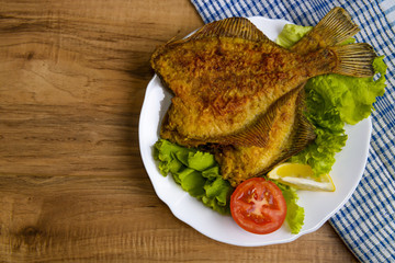 Fried Fish flounder on white plate with lettuce and lemon