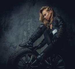 Fototapeta na wymiar Blonde female in leather clothes sits on a car's wheel .