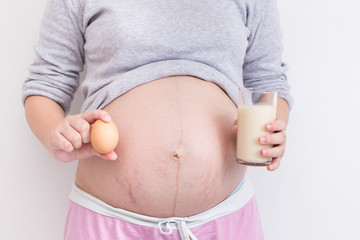 Pregnant woman's belly with egg and milk in her hand