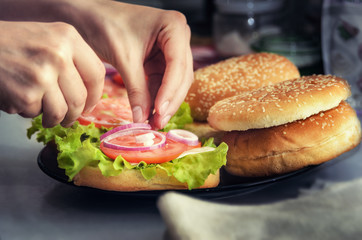 Chef  adds onion rings on hamburger. Cooking burger concept