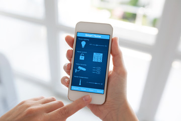 female hands holding white phone smart home screen against windo