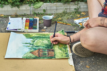 Naklejka premium Young girl is painting a watercolor picture sitting on the pavement 