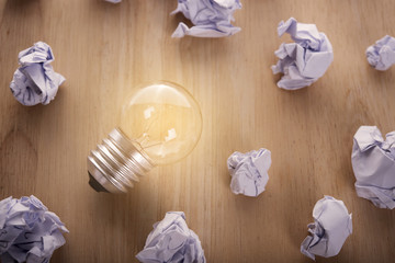 glowing lightbulb with crumpled paper ball on wooden table. concept for inspiration or idea under light bulb
