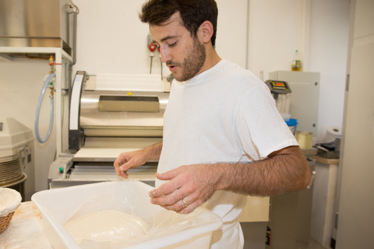 Cheerful baker man making dough at bakery