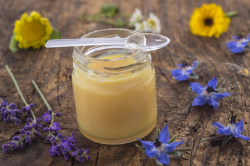 raw organic royal jelly in a small bottle with flowers on wooden board