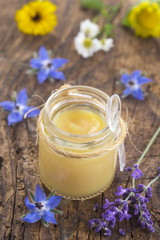 raw organic royal jelly in a small bottle with flowers on wooden board