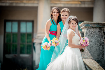 Naklejka premium Beautiful brunette bride and gorgeous bridesmaids with bouquets posing near stairs