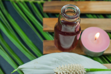 Bottle of aroma essential oil with flowers, candles in a spa setting - palm leaf background