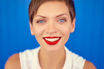 Haircut and red lipstick make up. Colorful portrait of smiling young woman. Blue background.