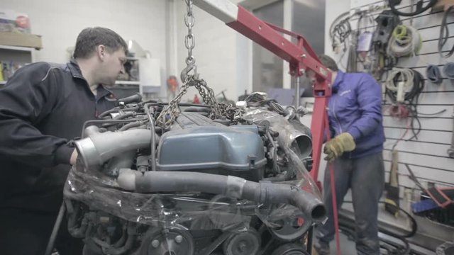 Experienced workers move the car engine