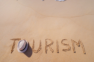 Vacation concept on the beach. Word Tourism written on the sand near the sea.