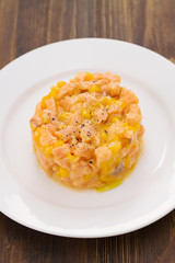 salmon with mango on white plate on brown wooden background