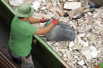  bricklayer mason worker depositing waste of bricks and tiles in rubble dumpster container in...