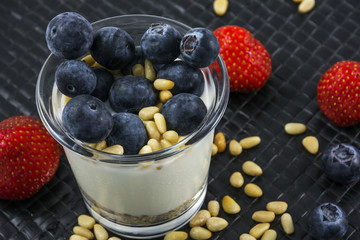 Natural yogurt with blueberries strawberries and pine nuts in glass on the black background