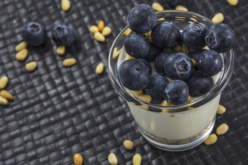 Glass of natural white yogurt with blueberries and pine nuts on the black background