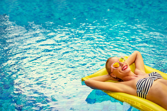 Enjoying suntan. Vacation concept. Slim young woman in bikini on the yellow air mattress in the swimming pool.