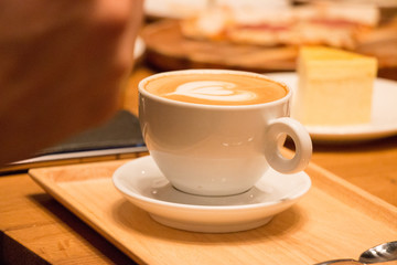 Coffee in white cup with coffee arts on the top on the wooden tray