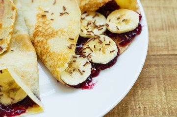 Sweet dessert: homemade thin pancakes with fresh banana slices, tasty fruit jam and chocolate flavoured strands