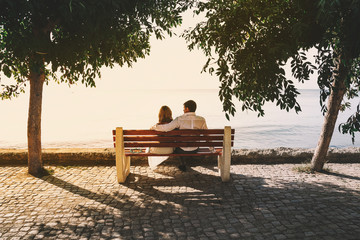 in love with a pair of man and woman sitting on a bench on the beach and watching the sea. Back view