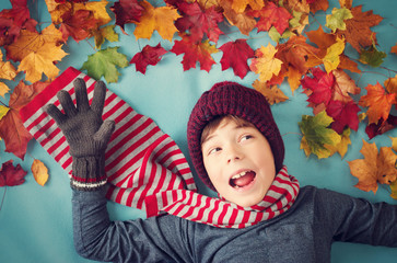 seven years old boy dreaming in autumn. Child in hat and scarf and maple leaves on blue background