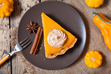 Festive Thanksgiving Homemade Pumpkin Pie with Whipped Cream and cinnamon on rustic background, top view. Autumn Decoration and rustic style.