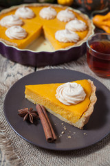 Festive Thanksgiving Homemade Pumpkin Pie with Whipped Cream on wooden rustic background with spices and tea