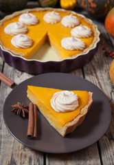 Festive Homemade Delicious Pumpkin Pie made for Thanksgiving with whipped cream, spices and autumn decoration. Rustic style.