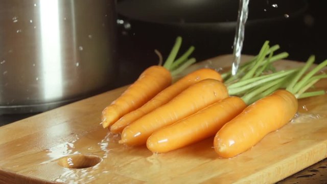 SLOW MOTION: Water stream falls on a carrots on a cutting board in a kitchen